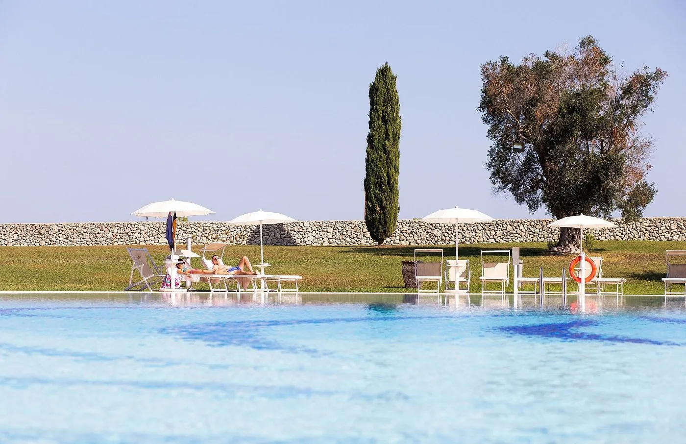 Piscina esterna con ospiti rilassati su lettini e muretto in pietra sullo sfondo