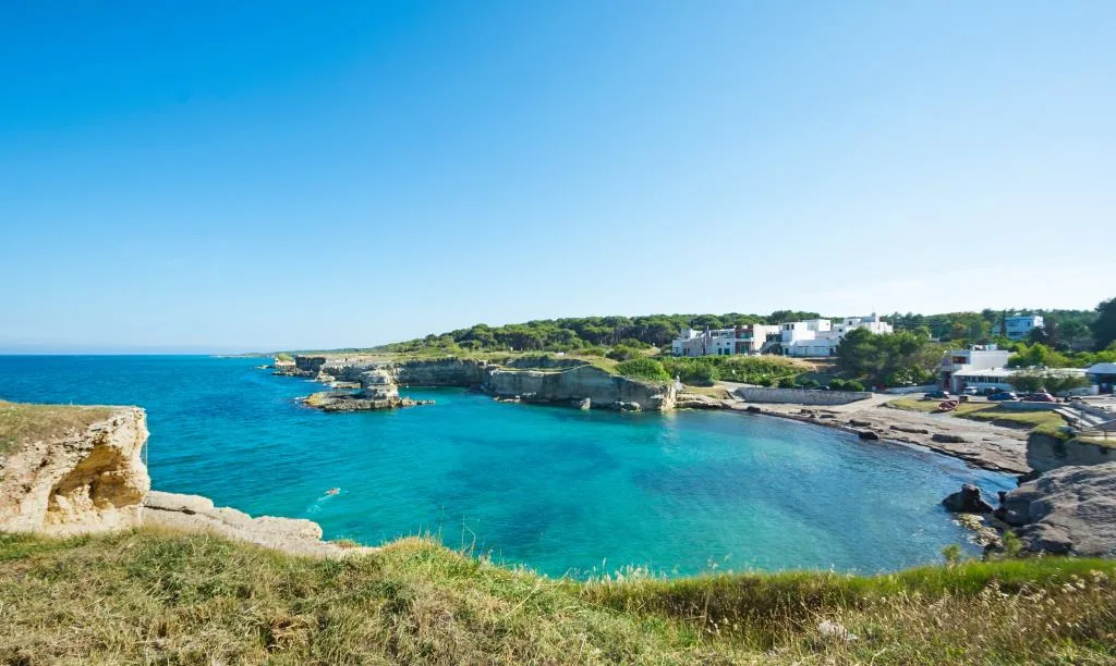 Baia con acque turchesi e costa rocciosa con case bianche immerse nel verde
