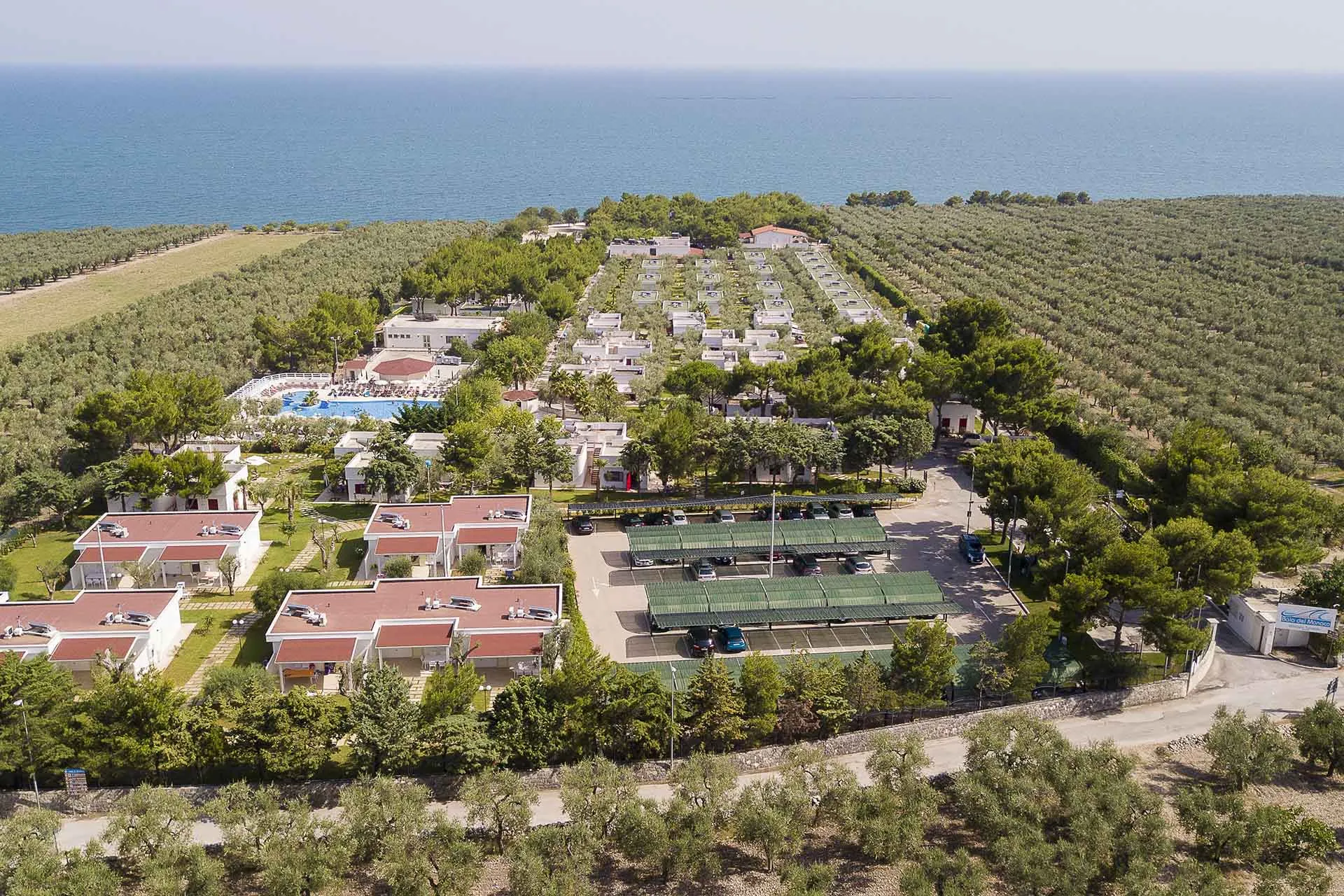 Panoramica aerea del villaggio turistico con piscina, parcheggio e bungalow vicino al mare