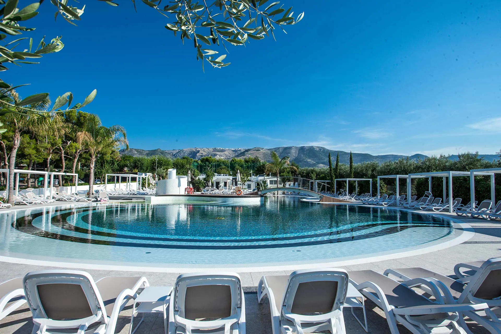 Piscina circolare con lettini bianchi e vista sulle montagne all'orizzonte