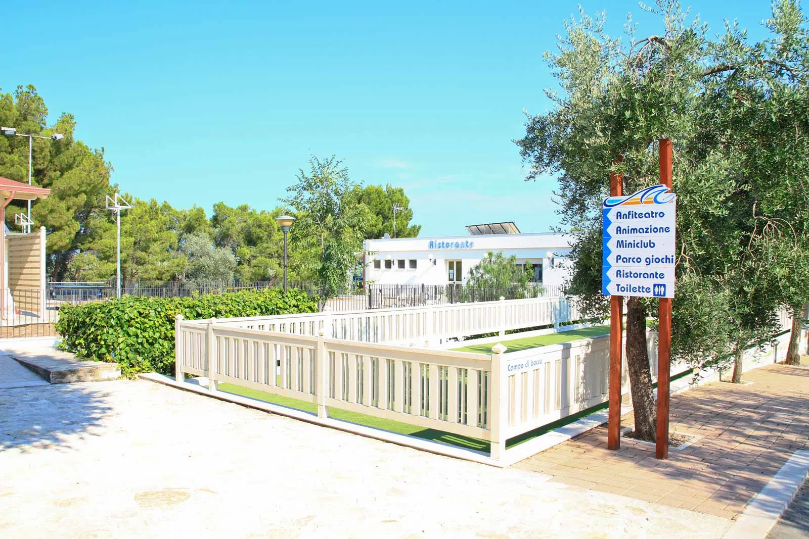 Area servizi del villaggio con campo da bocce e cartello indicatore tra gli ulivi