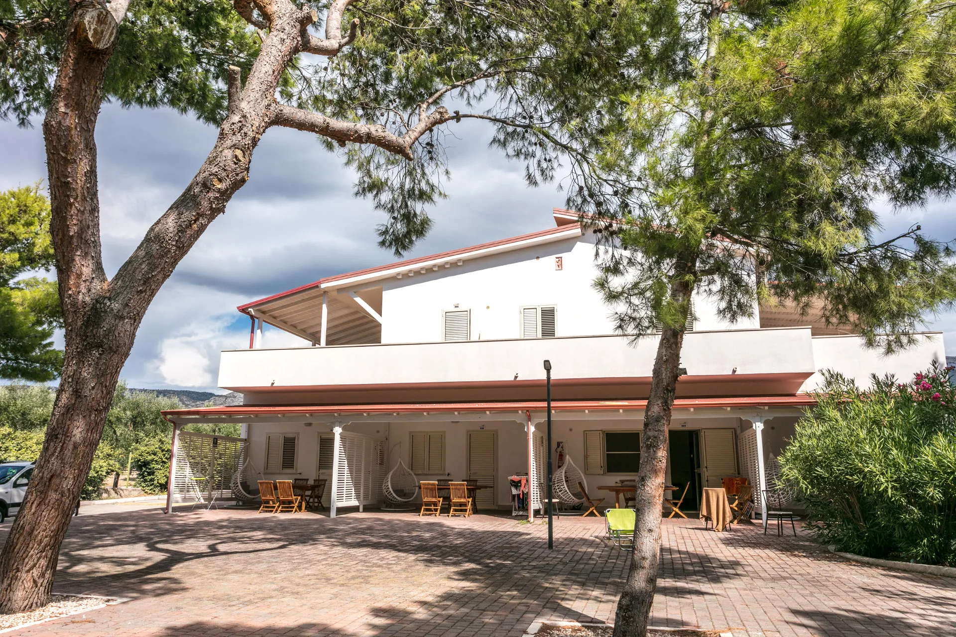 Esterno di un bungalow bianco a due piani con veranda, tavoli e poltrone sospese