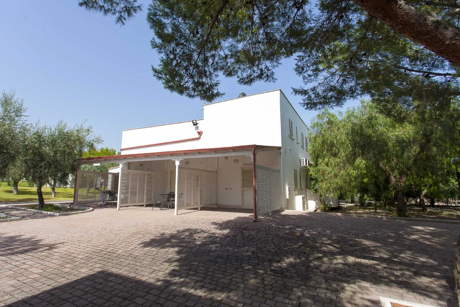 Edificio bianco dei servizi del villaggio con portico e tavolini tra gli ulivi