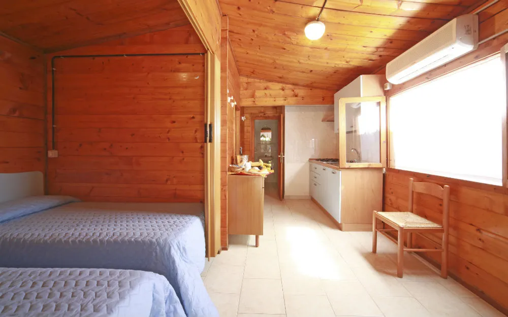 Interno di bungalow in legno con letti, angolo cottura e aria condizionata