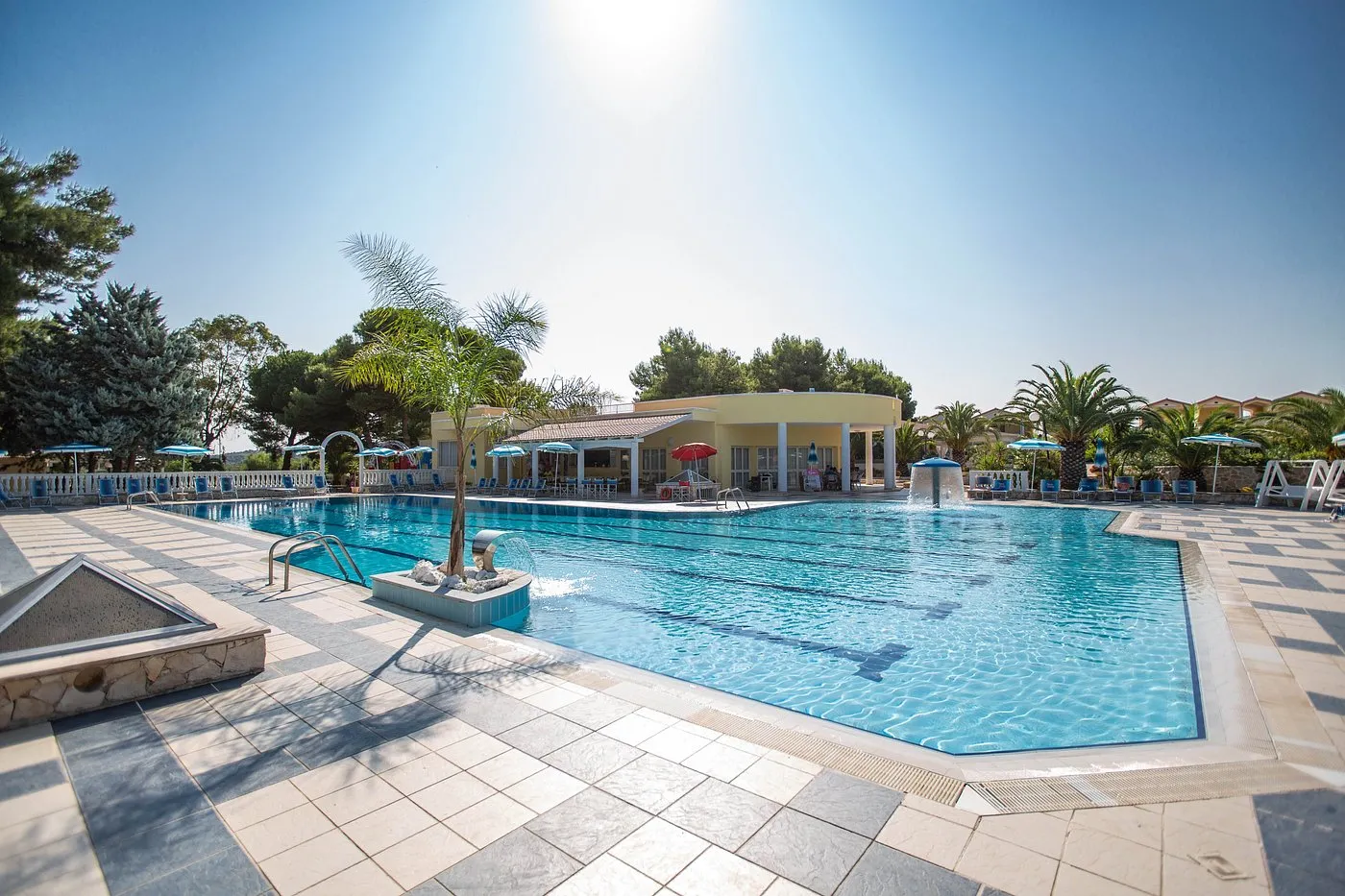 Piscina al tramonto con edificio giallo del resort, palme e ombrelloni azzurri