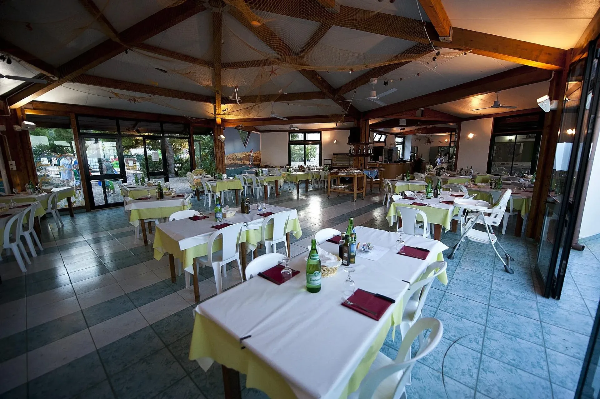 Sala ristorante interna con tavoli apparecchiati e soffitto in legno decorato con reti