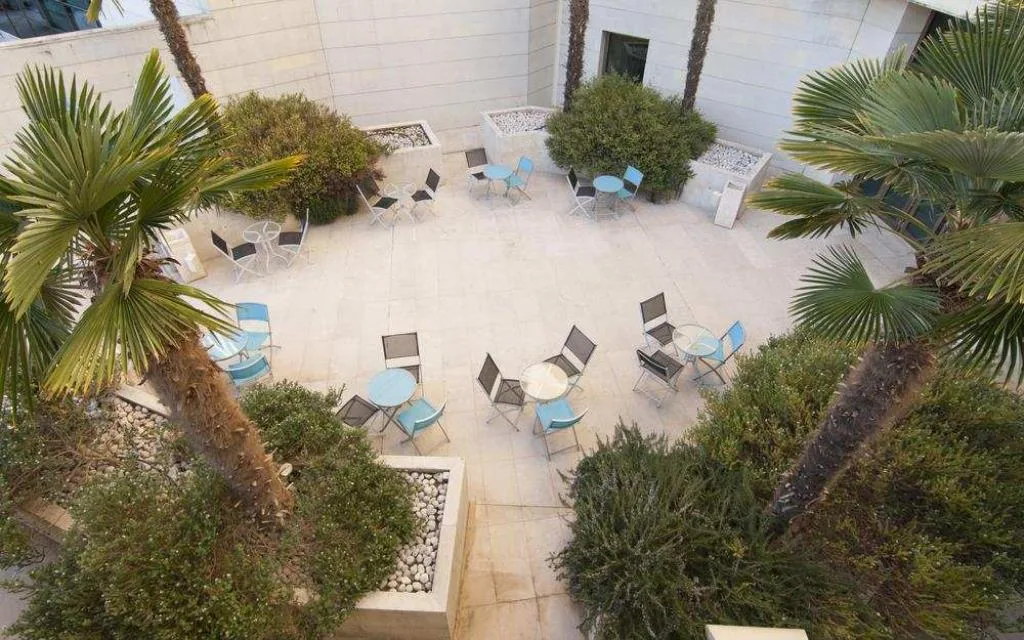 Cortile esterno con tavoli e sedie azzurre tra palme e piante mediterranee
