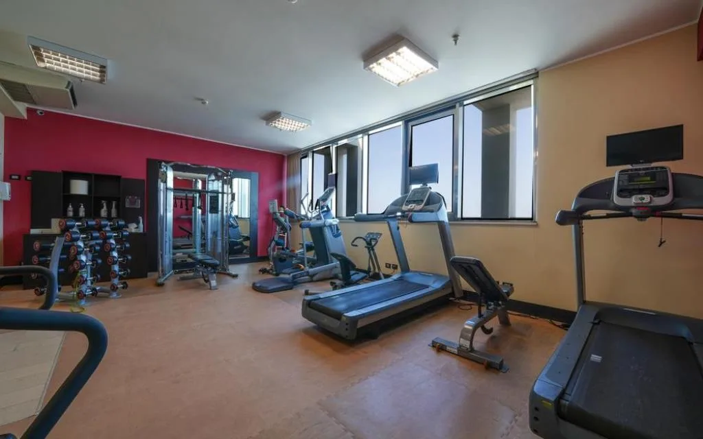 Palestra attrezzata con tapis roulant, pesi e macchinari cardio davanti alle finestre