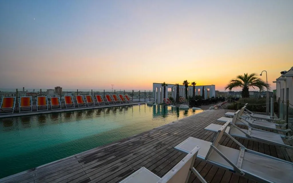 Piscina sul tetto con lettini e sdraio arancioni al tramonto con vista sulla città