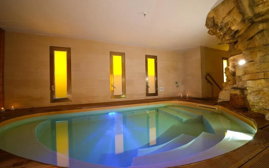 Piscina coperta con luci soffuse gialle e parete rocciosa decorativa