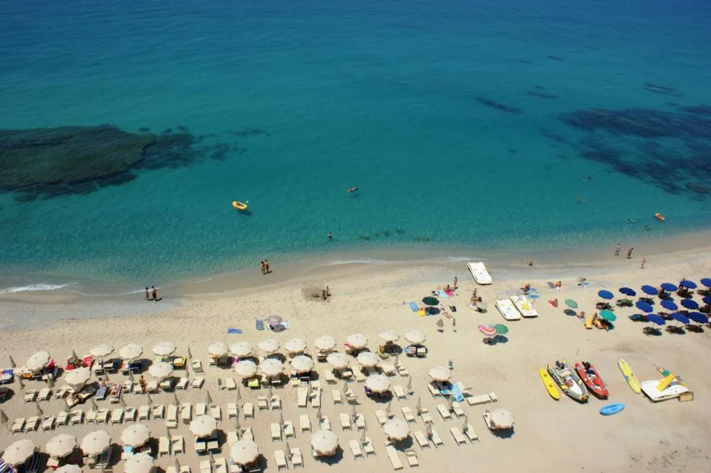 Veduta aerea della spiaggia con ombrelloni, lettini, pedalò e mare cristallino turchese