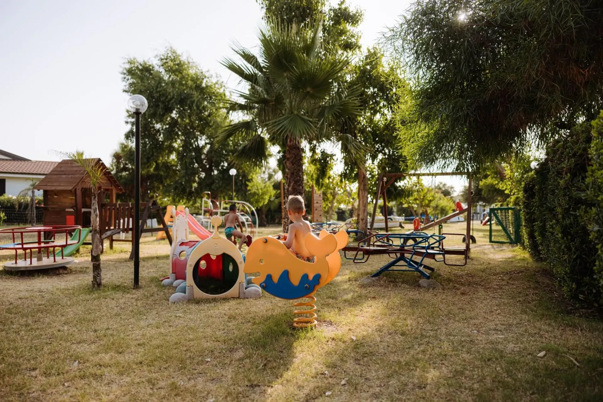 Area giochi per bambini all'aperto con scivoli, altalene e giostre tra palme e alberi