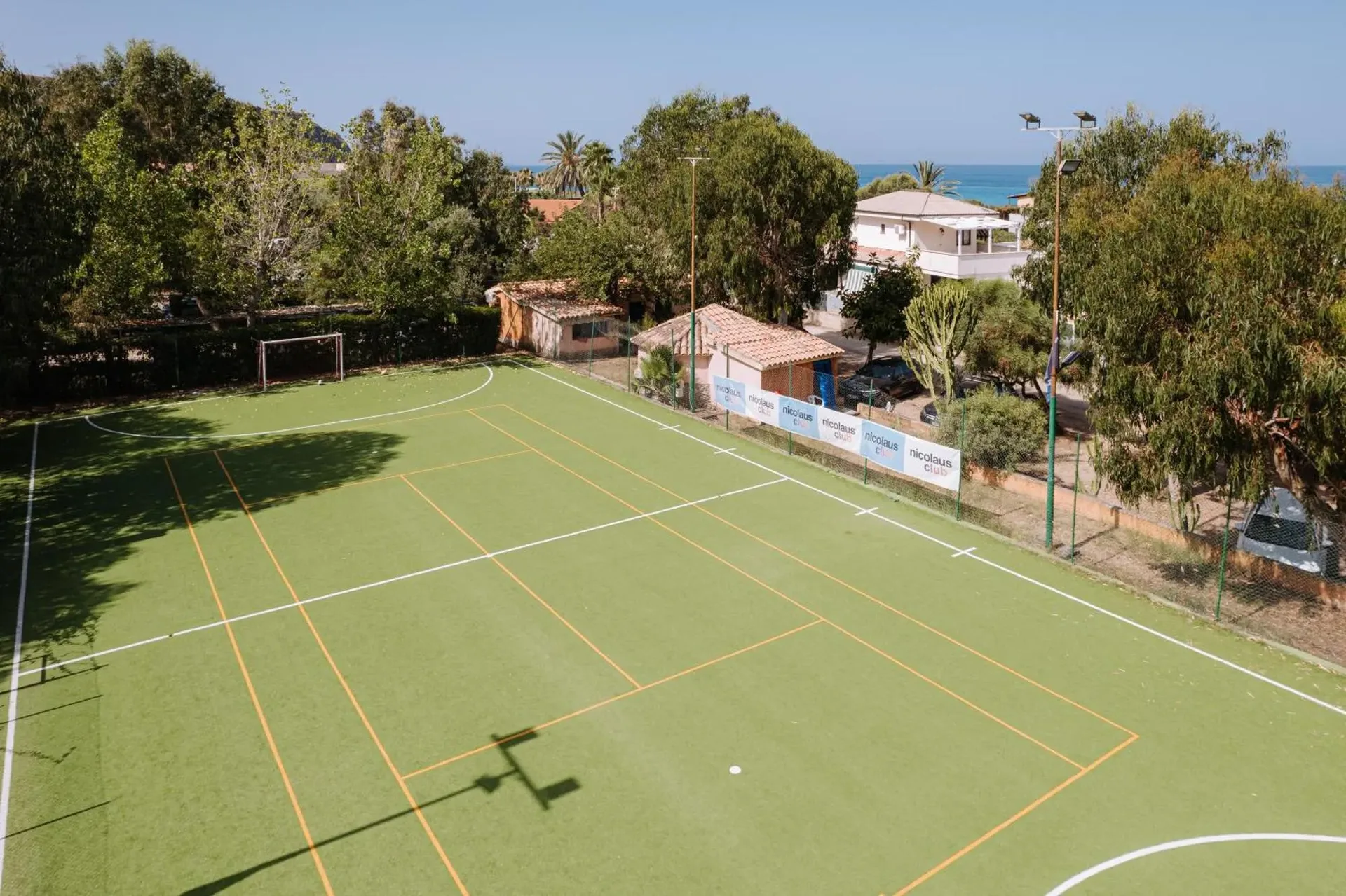 Campo sportivo polivalente in erba sintetica con vista sul mare e vegetazione circostante