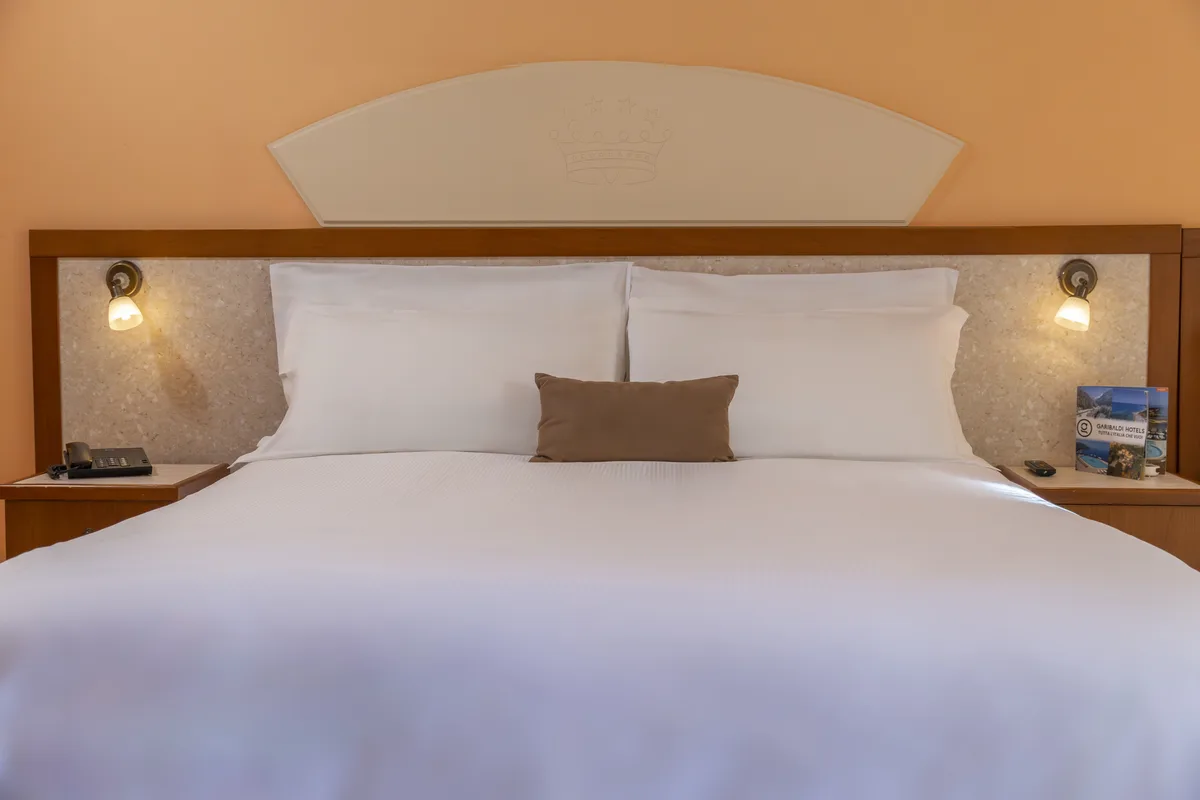 Letto matrimoniale con testiera in legno, lenzuola bianche e cuscino marrone