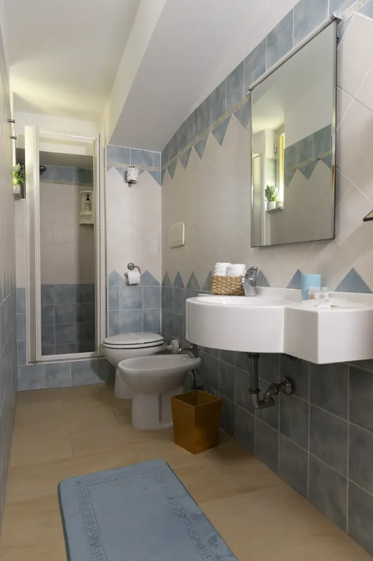 Bagno con piastrelle azzurre e bianche, doccia, lavabo, bidet e sanitari
