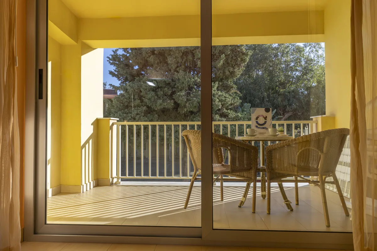 Vista dal balcone con tavolino, sedie in vimini e alberi attraverso ampia vetrata