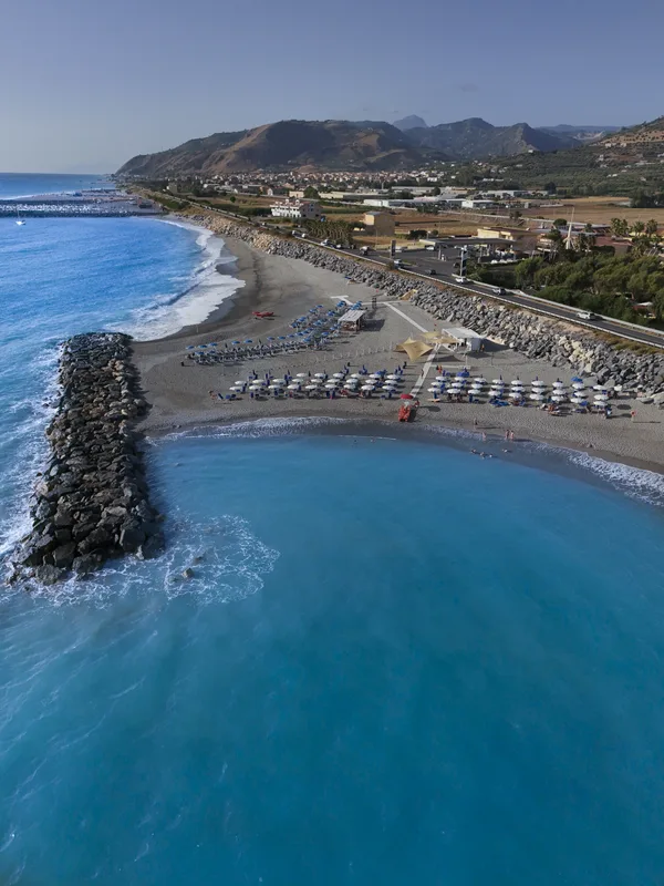 Veduta aerea della spiaggia attrezzata con ombrelloni, mare azzurro e costa montuosa