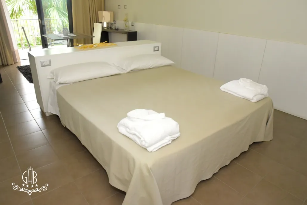 Camera luminosa con letto matrimoniale, asciugamani arrotolati e scrivania con vista giardino