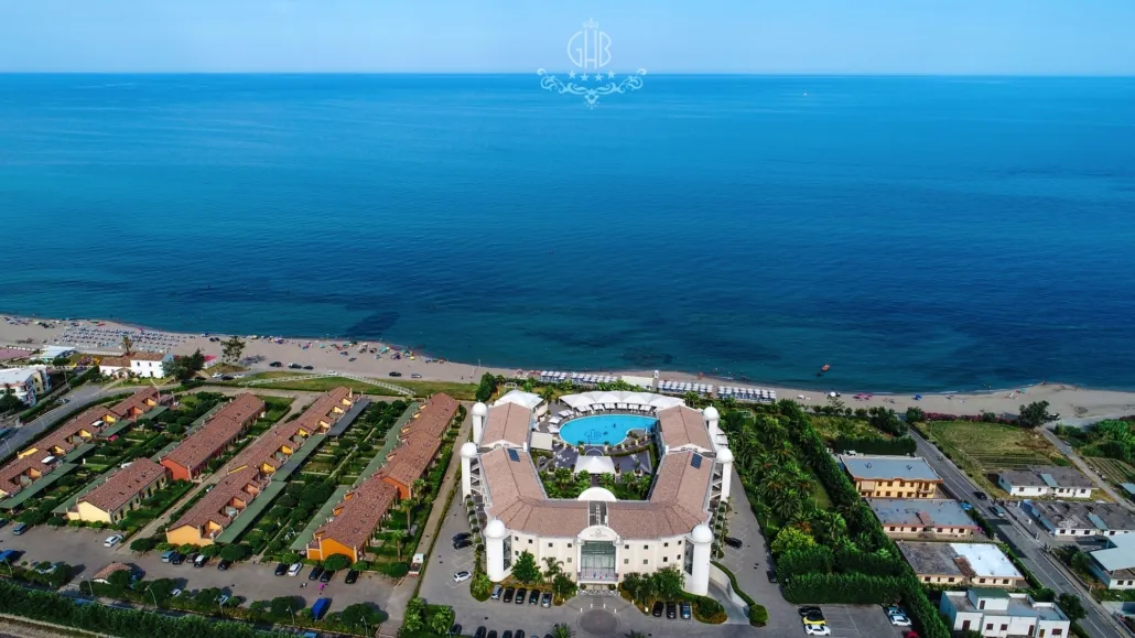 Vista aerea dell'hotel fronte mare con piscina, spiaggia e mare blu all'orizzonte