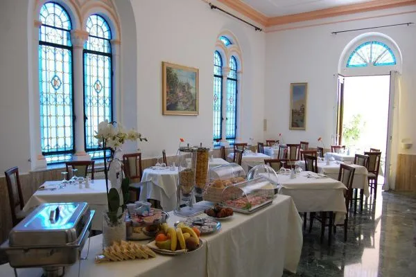 Sala colazione con buffet di frutta e dolci, vetrate ad arco e tavoli eleganti