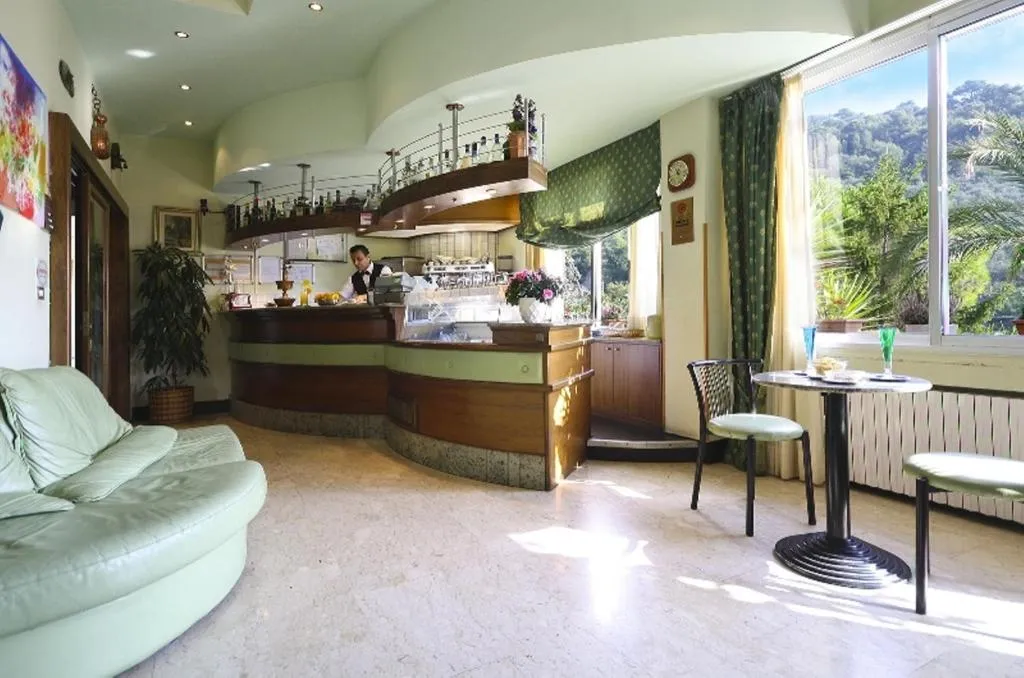 Bar dell'hotel con bancone in legno, divano e ampia vetrata sul verde
