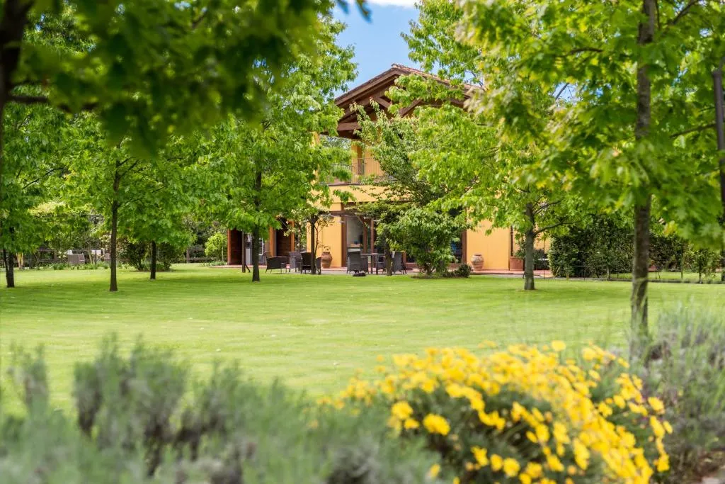 Edificio giallo immerso nel verde tra alberi e fiori gialli