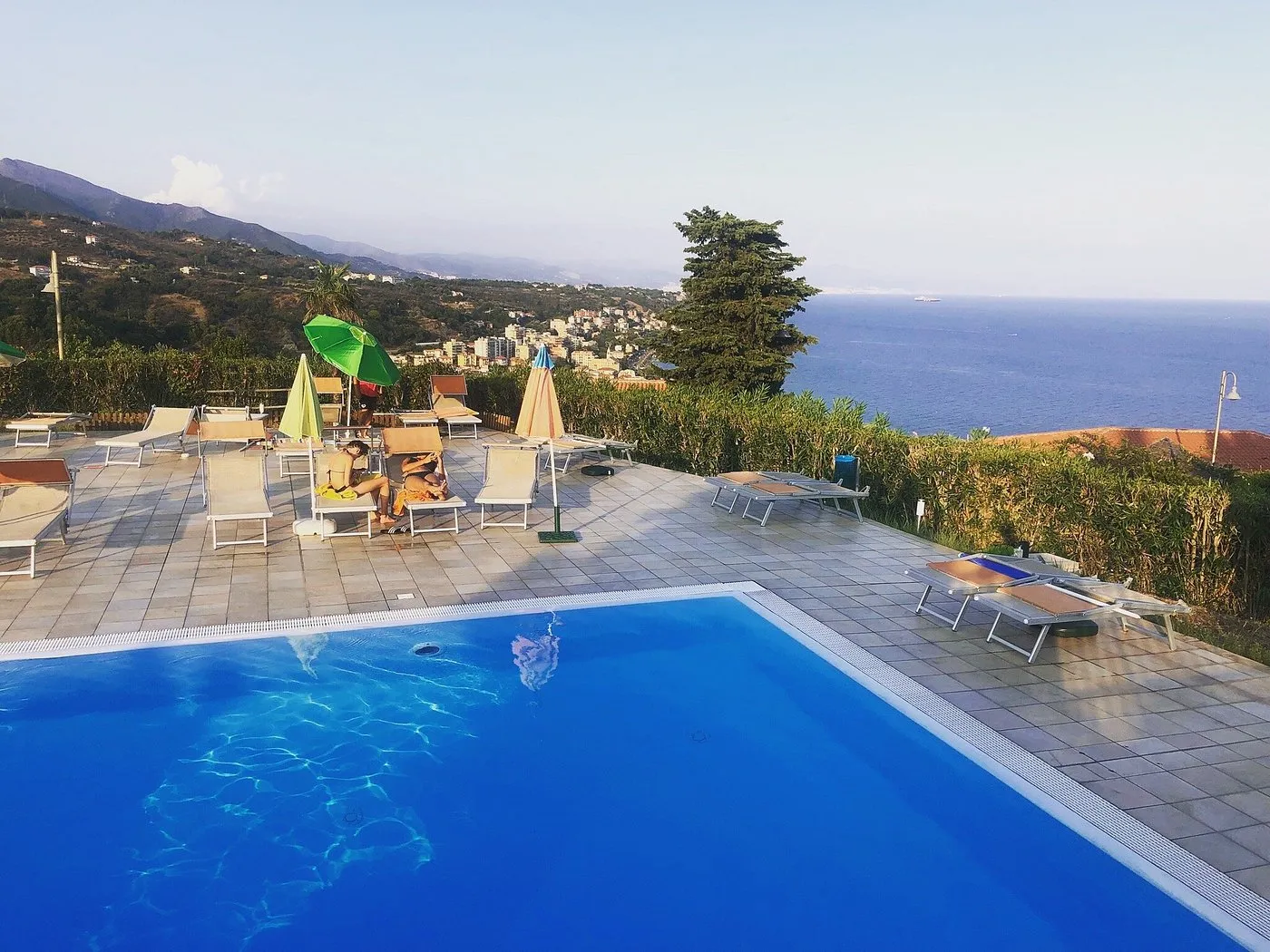 Piscina con lettini e ombrelloni affacciata sul mare e le montagne