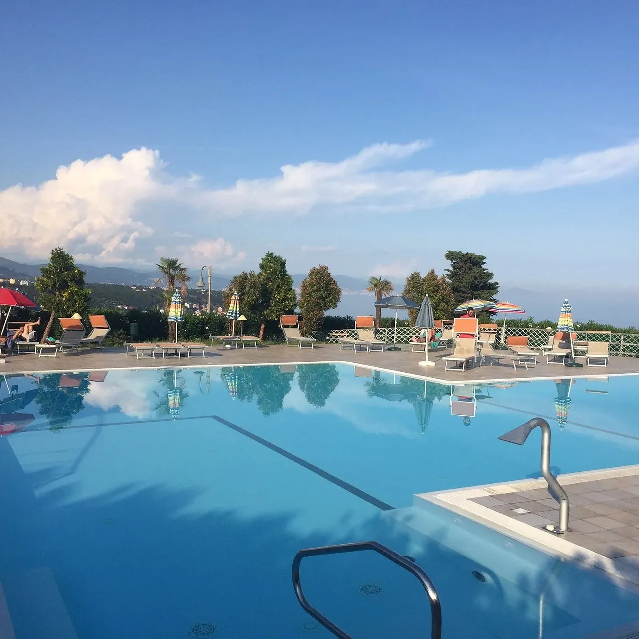 Ampia piscina con lettini e ombrelloni colorati e vista mare