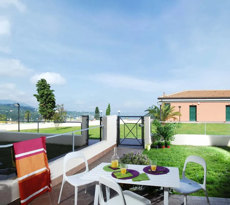 Terrazza con tavolo e sedie bianche affacciata sul giardino e sul mare