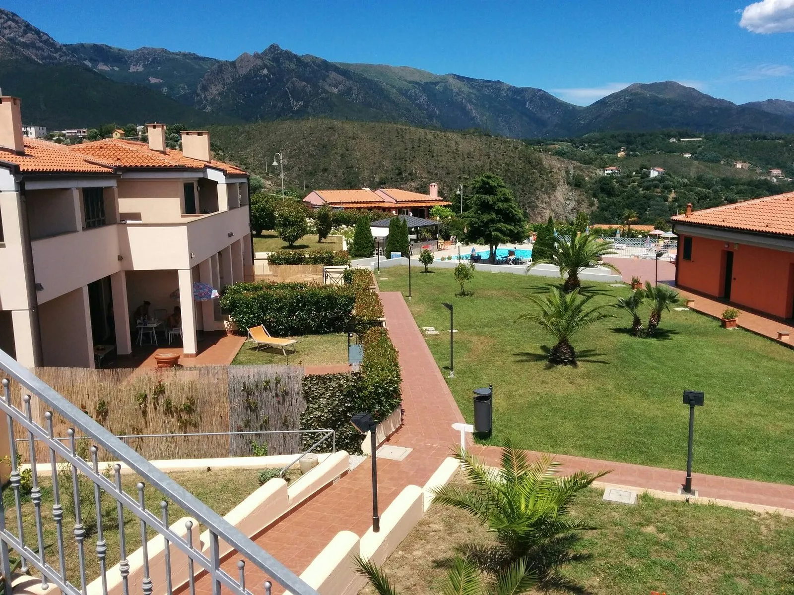 Vista dal balcone su giardini, piscina e montagne del residence