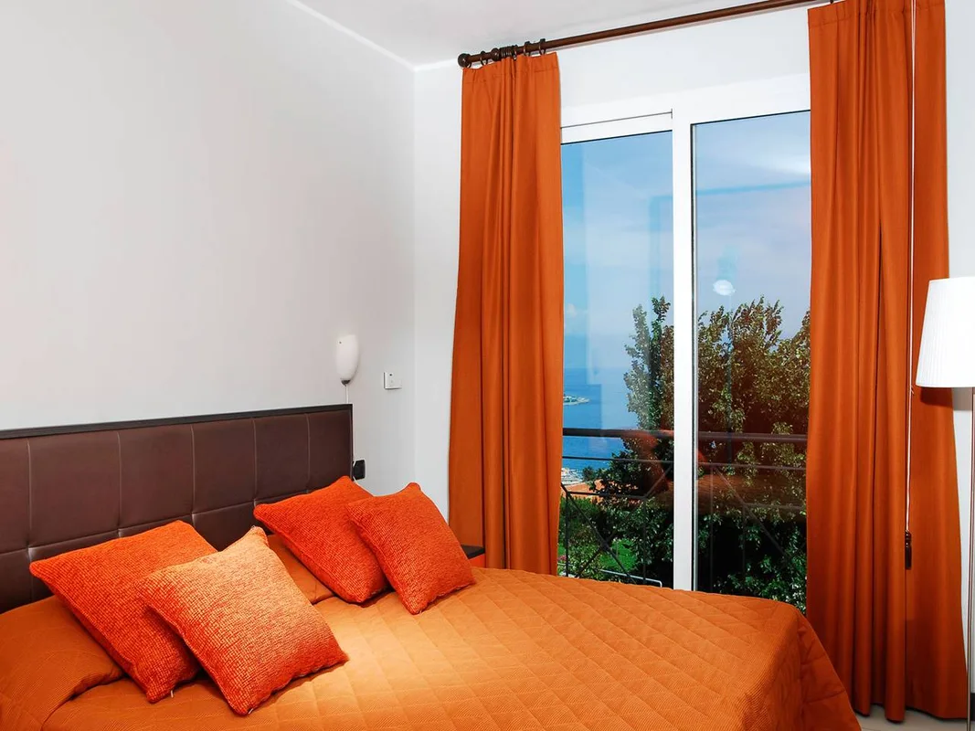 Camera da letto con cuscini arancioni e vista mare dalla finestra