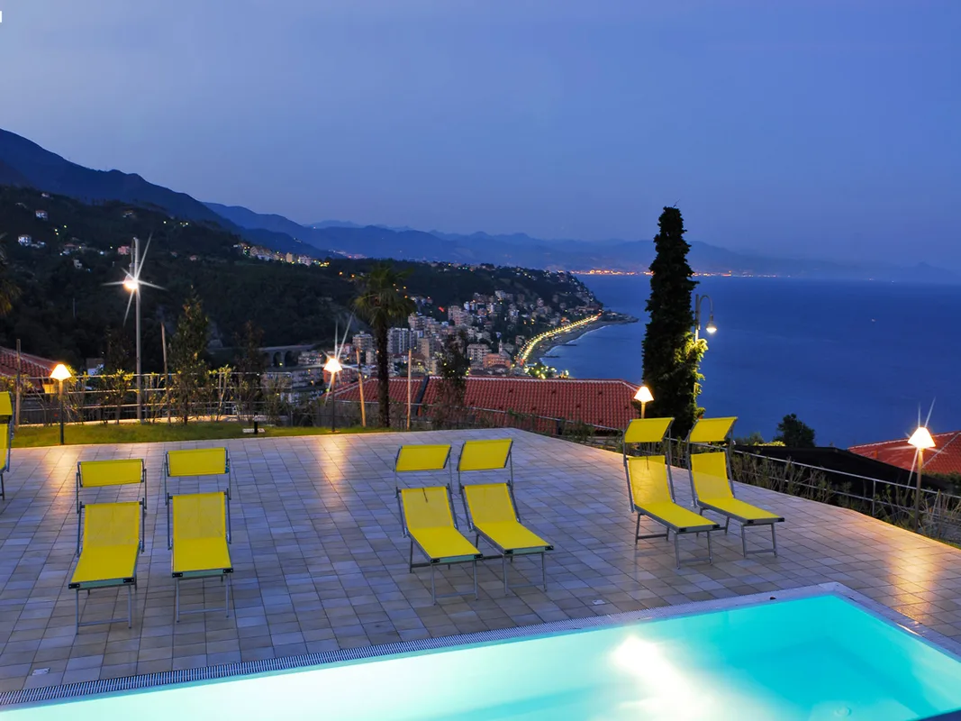 Piscina illuminata al crepuscolo con lettini gialli e vista sulla costa