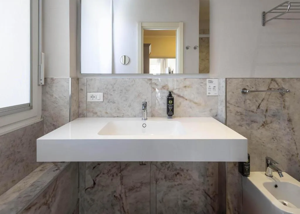 Bagno con lavabo bianco sospeso, specchio e rivestimenti in marmo
