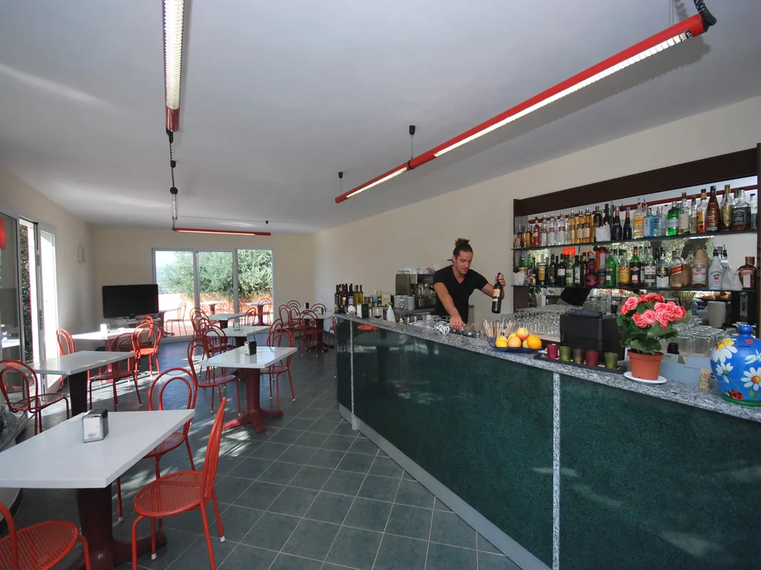 Sala bar interna con bancone verde, tavoli e sedie rosse e barista al lavoro