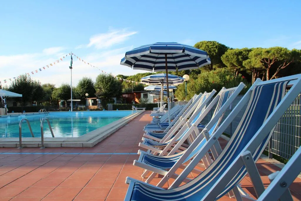 Lettini a righe blu e ombrelloni accanto a una piscina con pini sullo sfondo