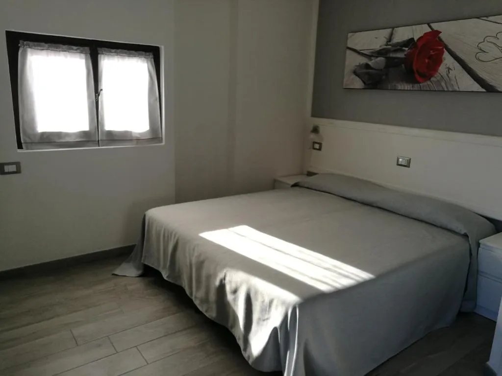 Camera da letto matrimoniale con copriletto grigio, quadro decorativo e finestra con tende bianche