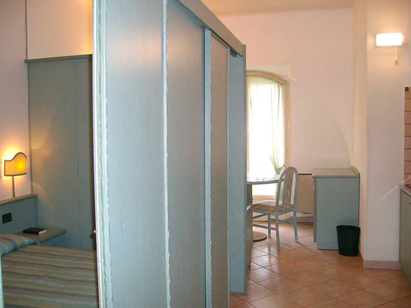 Interno di camera con armadi azzurri, letto e angolo cottura