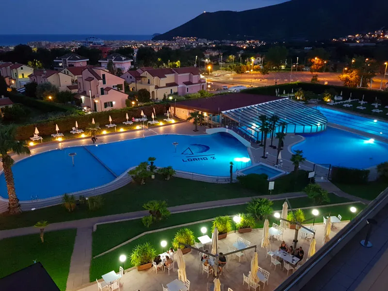 Piscine del resort illuminate di sera con terrazza e tavoli