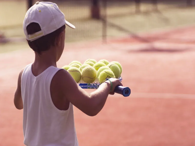 Bambino con racchetta e palline da tennis sul campo