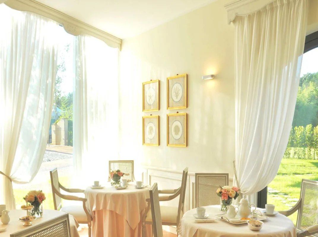 Sala colazione luminosa con tavoli apparecchiati, tende bianche e vista sul giardino