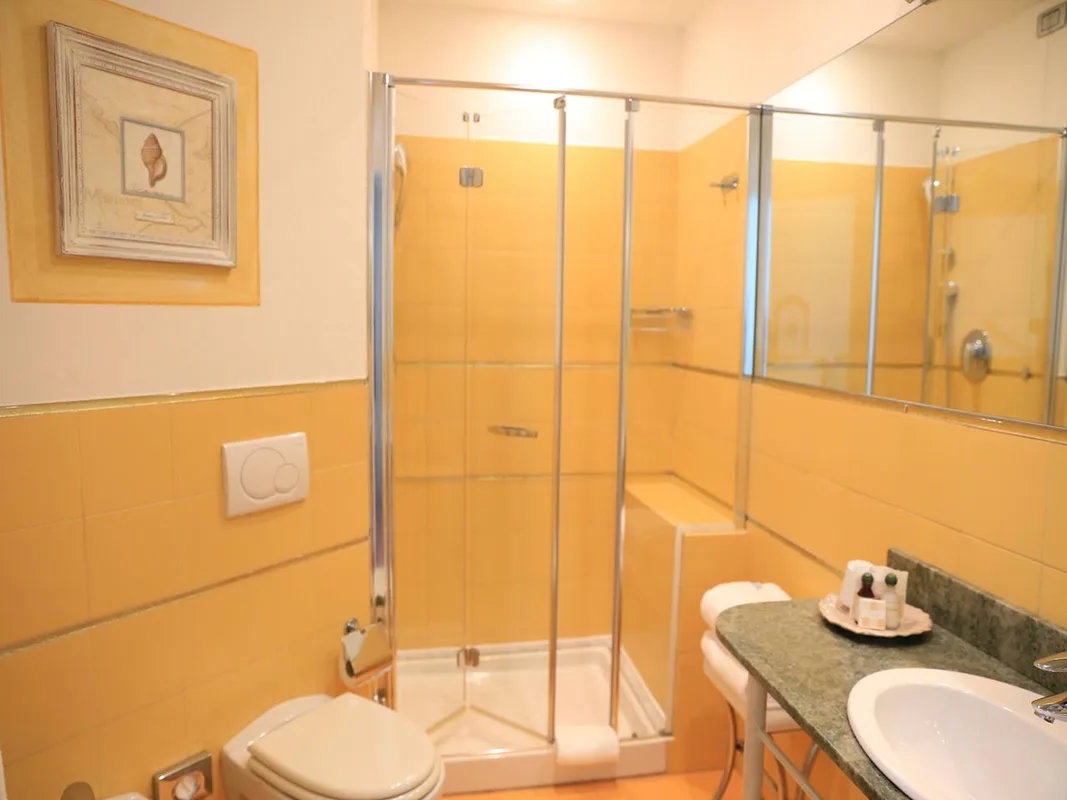 Bagno con box doccia in vetro, piastrelle gialle e lavabo con specchio