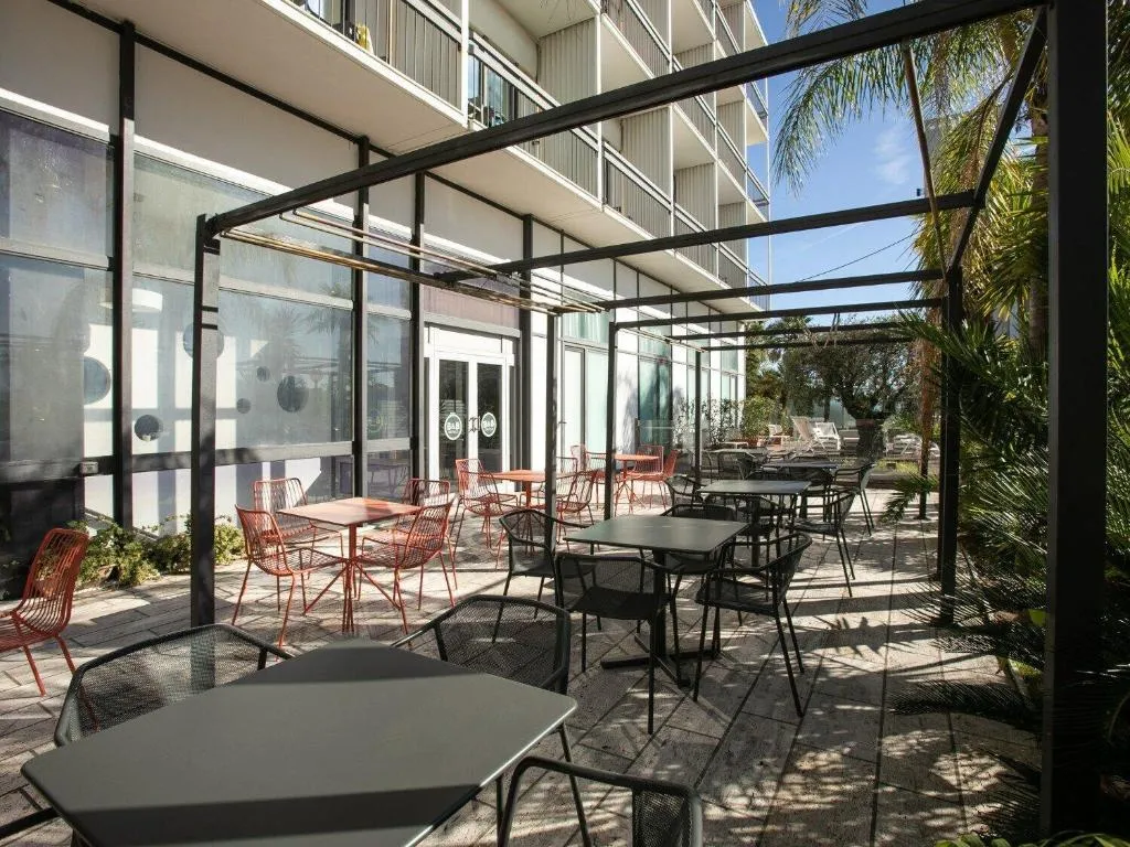 Terrazza esterna con tavoli, sedie colorate e vegetazione tropicale accanto all'edificio dell'hotel