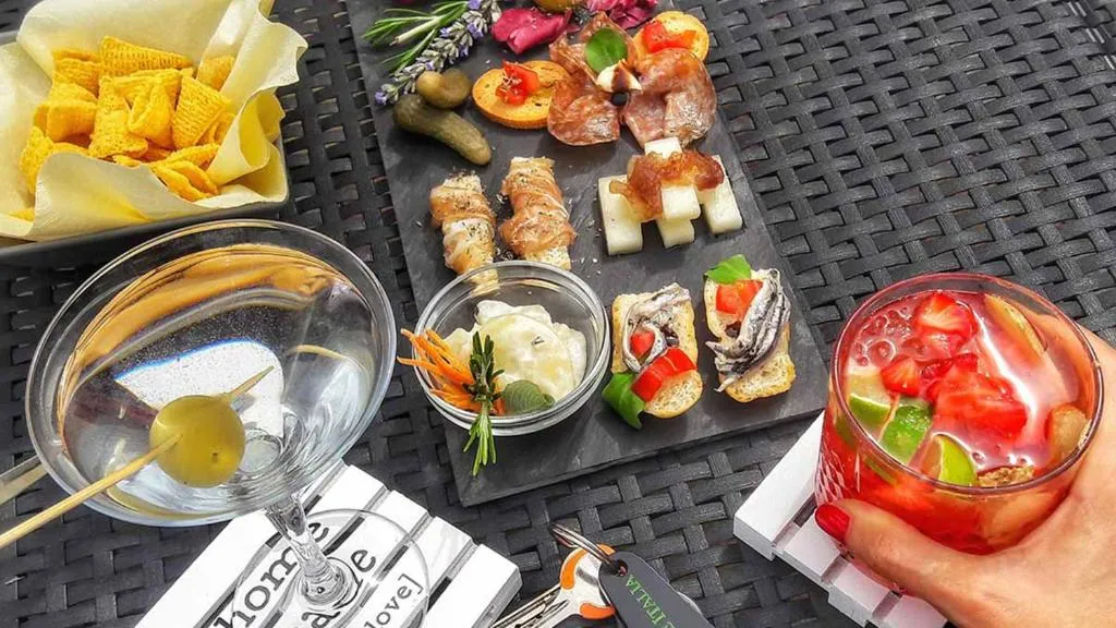Aperitivo con tagliere di salumi e stuzzichini, cocktail e snack su tavolo in rattan