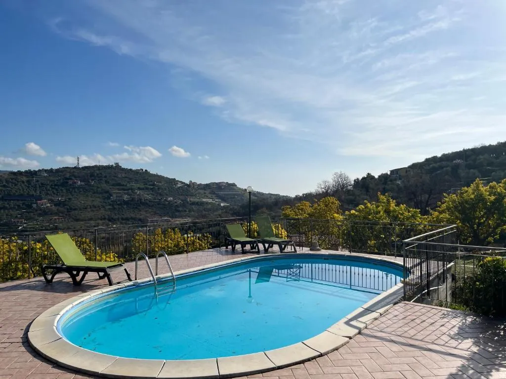 Piscina con lettini verdi e vista panoramica sulle colline con mimose