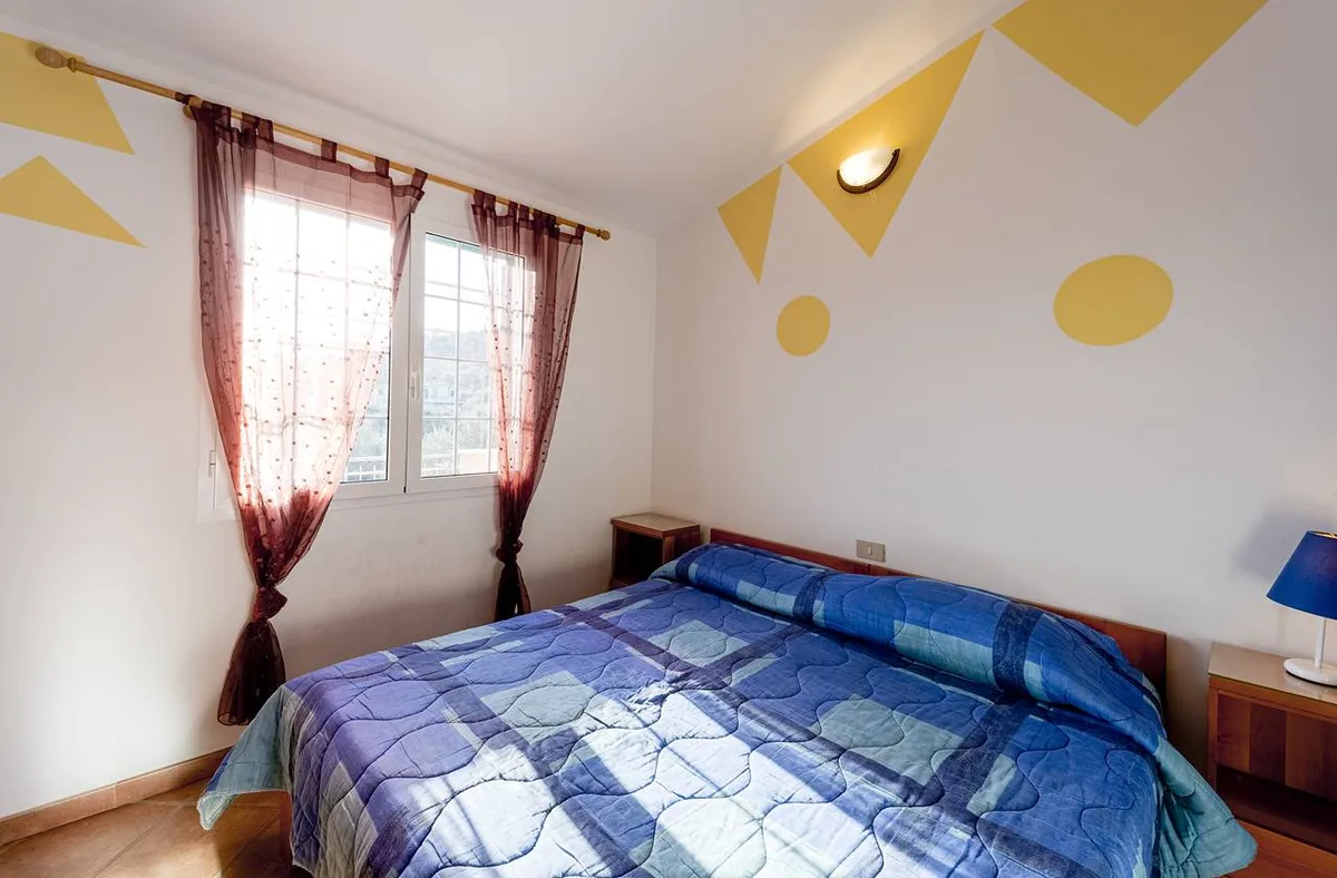 Camera da letto con pareti decorate gialle, finestra con tende e letto matrimoniale blu