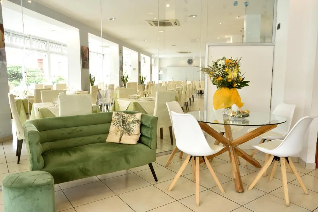 Area lounge con divano verde, tavolo in vetro e sala ristorante