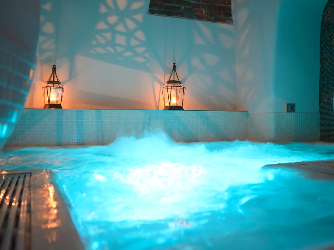 Vasca idromassaggio con acqua in movimento illuminata di azzurro e lanterne