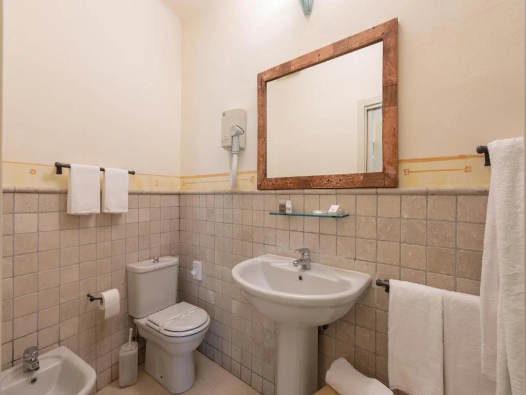 Bagno con piastrelle beige, lavabo, wc, bidet e specchio con cornice in legno