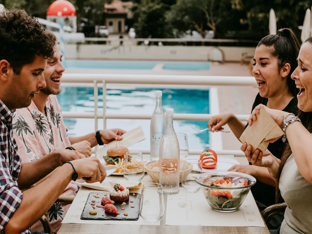 Gruppo di amici sorridenti che pranzano a un tavolo accanto alla piscina
