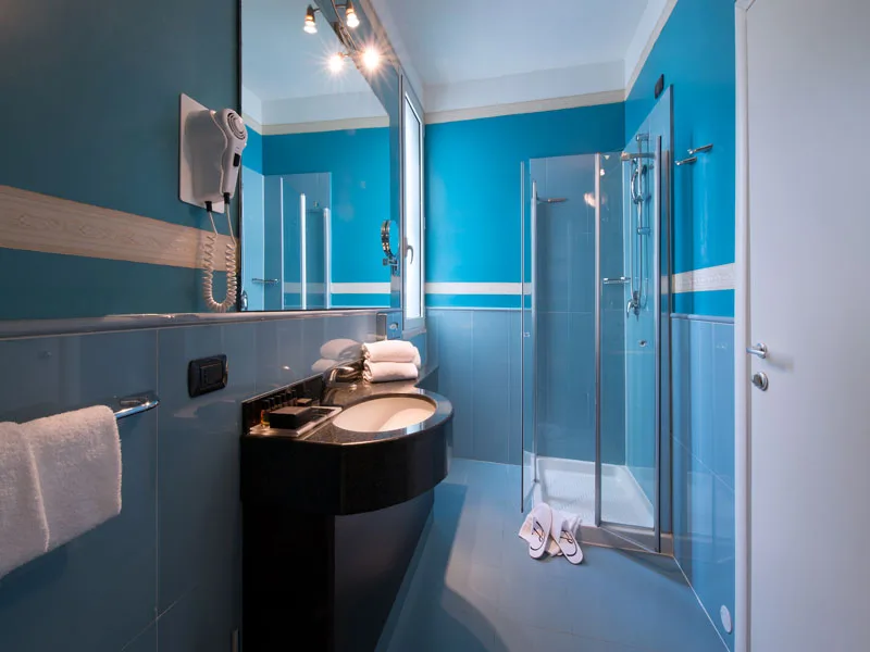Bagno moderno azzurro con doccia in vetro, lavabo nero e specchio